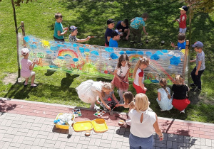 Dzieci w ogrodzie malują wiosenny obraz na dużym arkuszu folii, widok z gówy